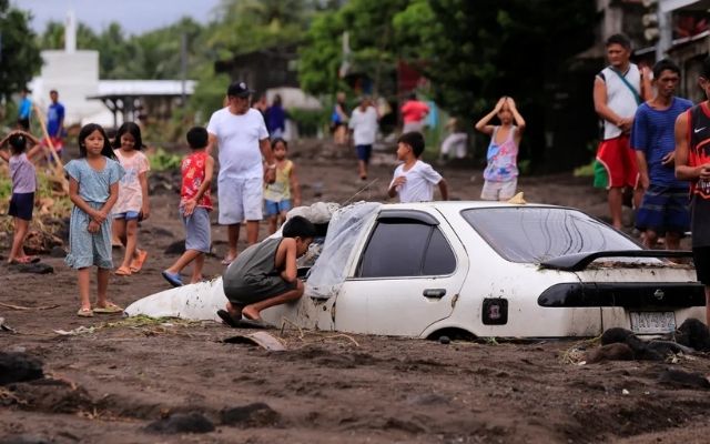 Residents look at a car covered in volcanic ash due to heavy rains