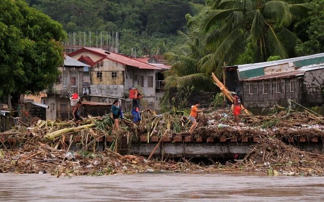 Residents cross a bridge filled with debris following heavy rains