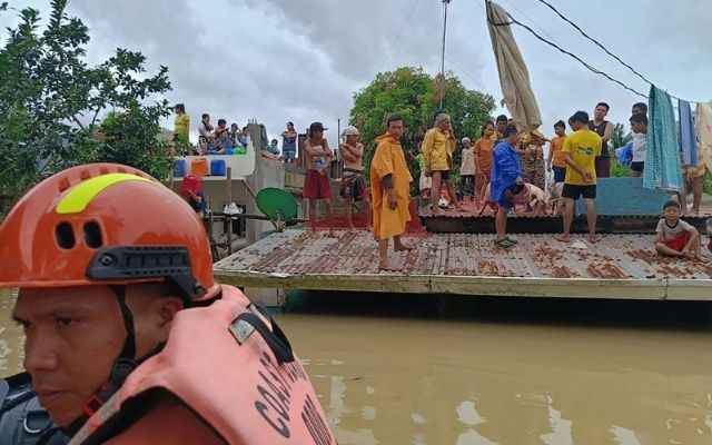 Residents stand on the rooftops of their inundated houses